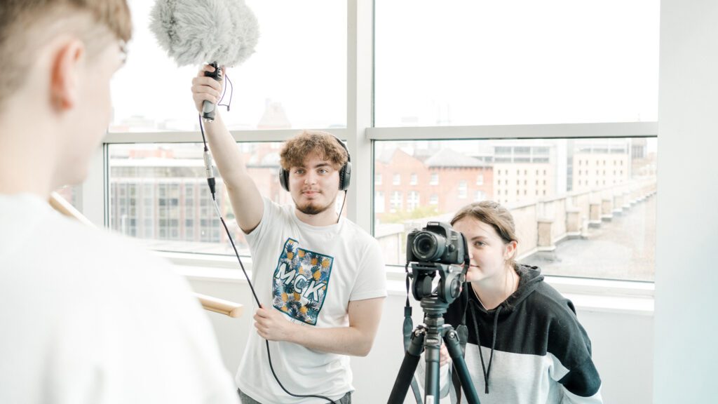 A trio of film students, one male student recording sound, a female student filming and the second male student is the subject
