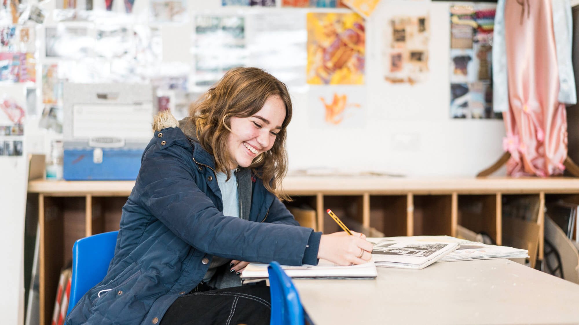Female student sat at desk writing and smiling