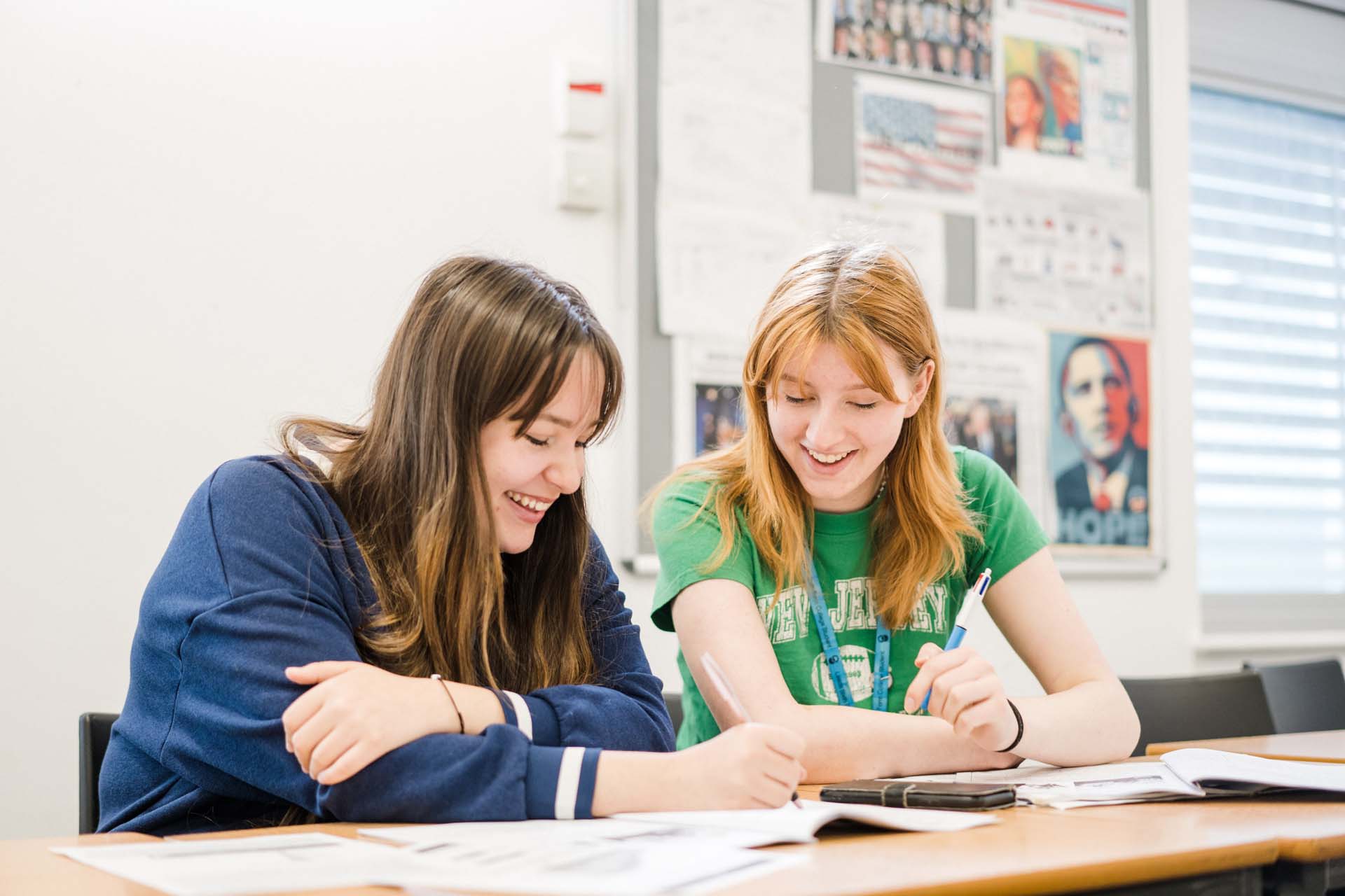 Two Leeds Sixth Form students working together taking notes and writing in their books sat at their desk smiling