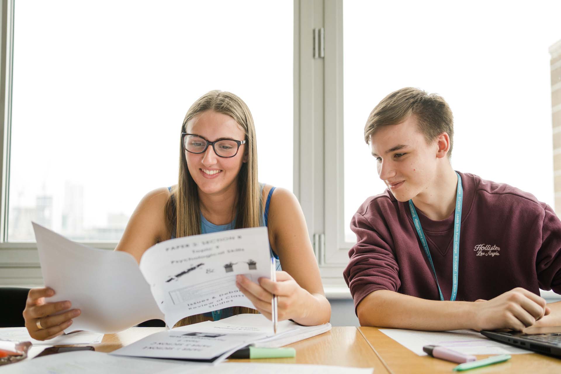 Two Leeds Sixth Form College students sitting on their desk reading through a book