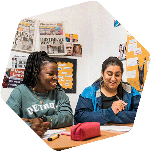 Two female students sitting in classroom having discussion and smiling
